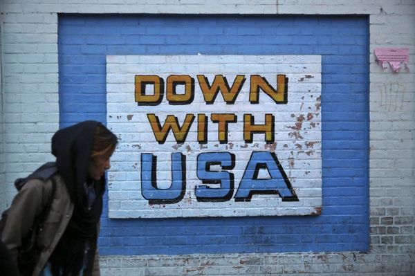 A woman walks past an anti-U.S. mural, written on ...
